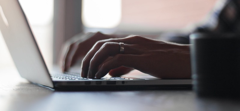 Hands typing on a laptop keyboard beside a window